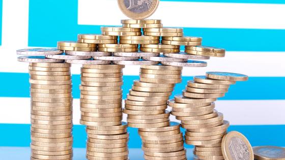 Precarious piles of euro coins with Greek flag in background